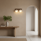 Two-dome travertine wall light from Clérachic, lit on a rough sand-coloured plaster wall beside an arched doorway and a wooden console.