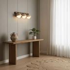 Three travertine domes on a walnut bar, lit over a wooden console with a clay vase, beside sheer curtains; a Clérachic wall light.