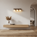 Three lit domes on a dark wood bar, a Clérachic wall light above a floating oak shelf with dried pampas grass and an arched doorway.