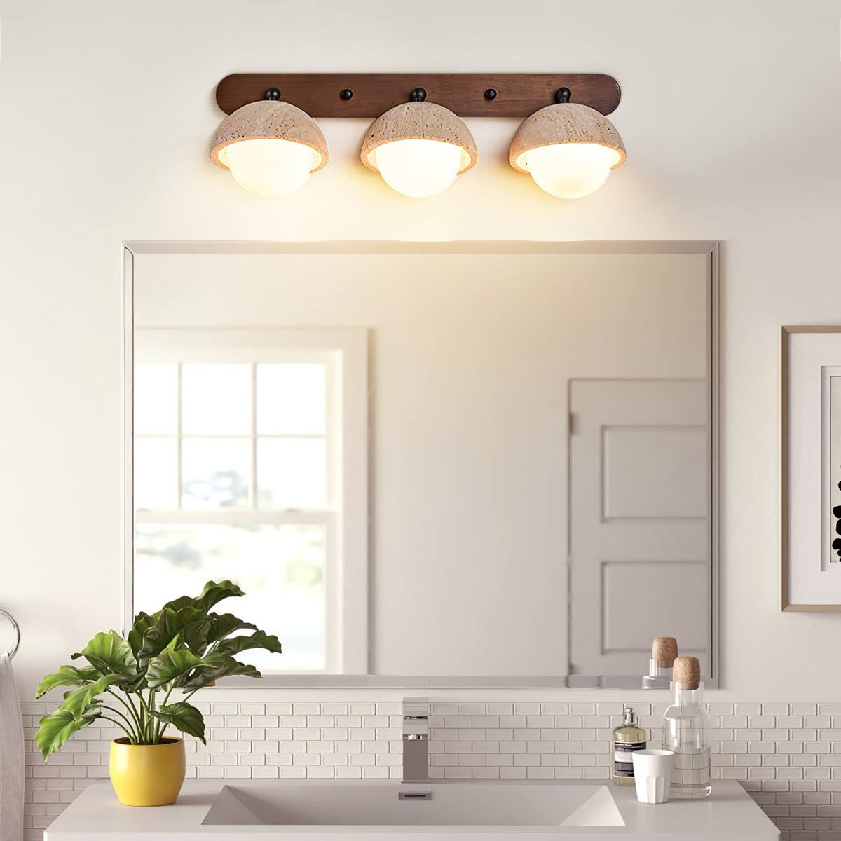 Close view of the three travertine domes and walnut bar of this Clérachic wall light, lit above a bathroom mirror.