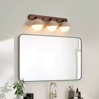 Travertine domes with warm light under them, on a walnut bar above a black-framed mirror; a Clérachic bathroom wall light.