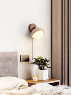 Travertine dome wall light from Clérachic with a pull chain, above a bedside table with a plant in a white pot and a lit candle.