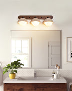 Clérachic three-dome wall light seen lit above a wide mirror, with a brick-tile backsplash and a sink in a walnut vanity.