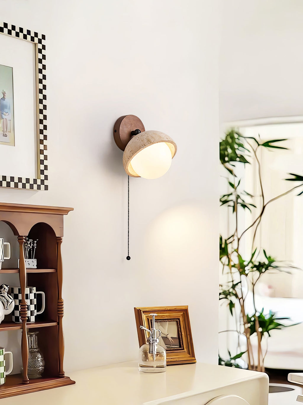 Pull-chain Clérachic wall light with a travertine dome, beside a framed checkered picture and a wooden shelf with cups and a photo.