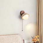 Close crop of a travertine dome wall light from Clérachic, lit above a cane headboard, with a bunch of orange flowers at the edge.
