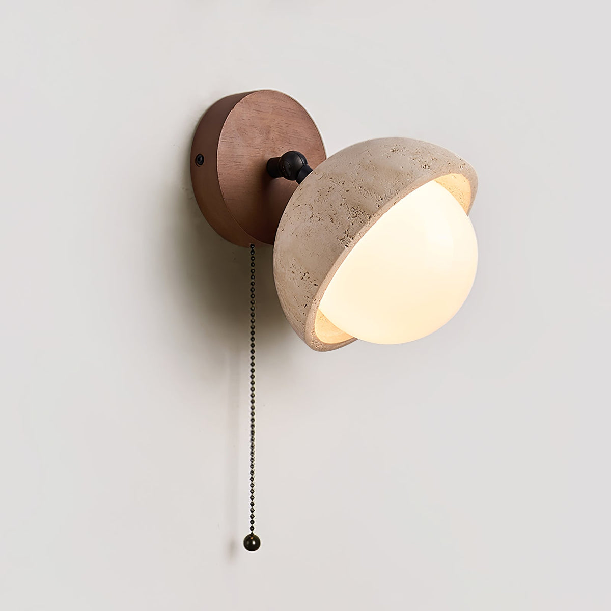 Large close view of the travertine half-dome shade, white glass globe and walnut backplate on this Clérachic wall light, with its chain.