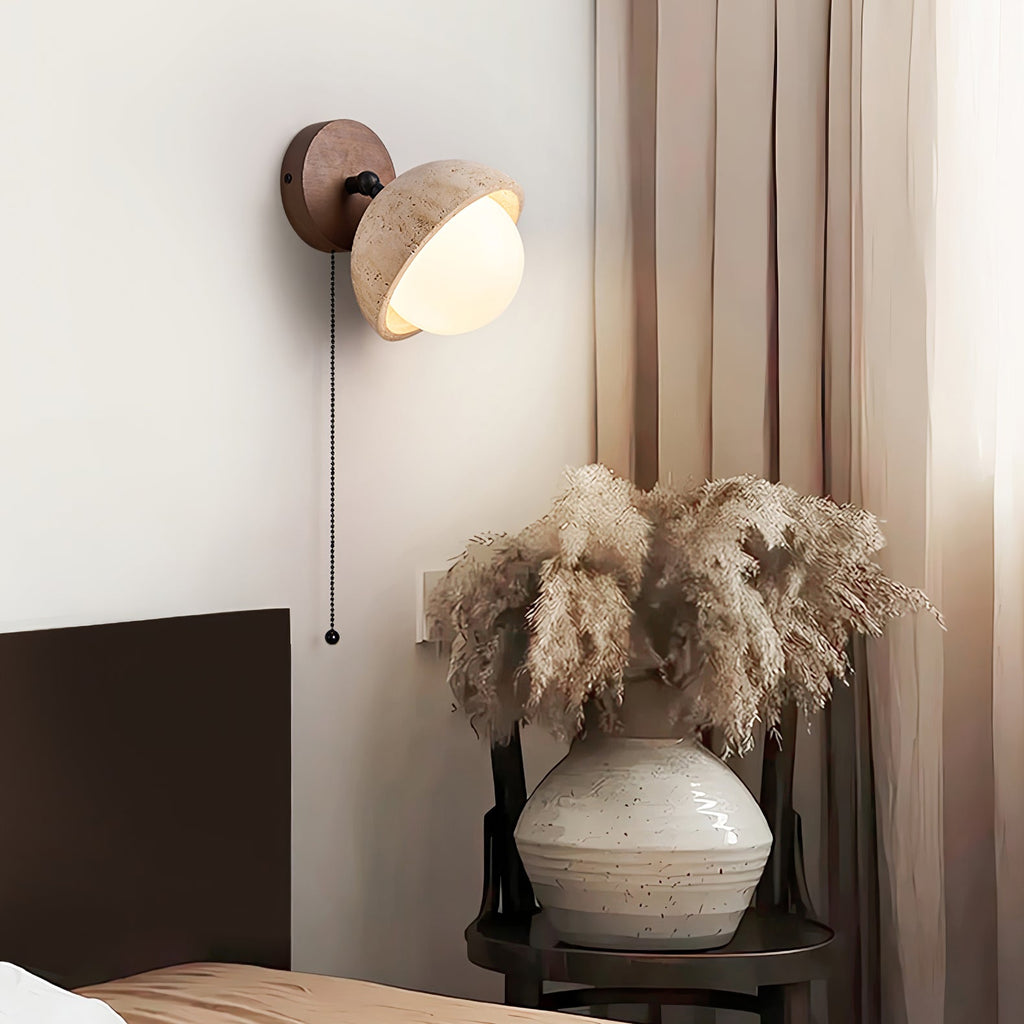 Clérachic wall light with a travertine dome and pull chain, near a tall vase of pampas grass and a sand-coloured curtain.