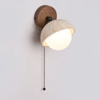 Side view of the travertine dome and white glass globe on this Clérachic wall light, with its walnut round backplate and pull chain.