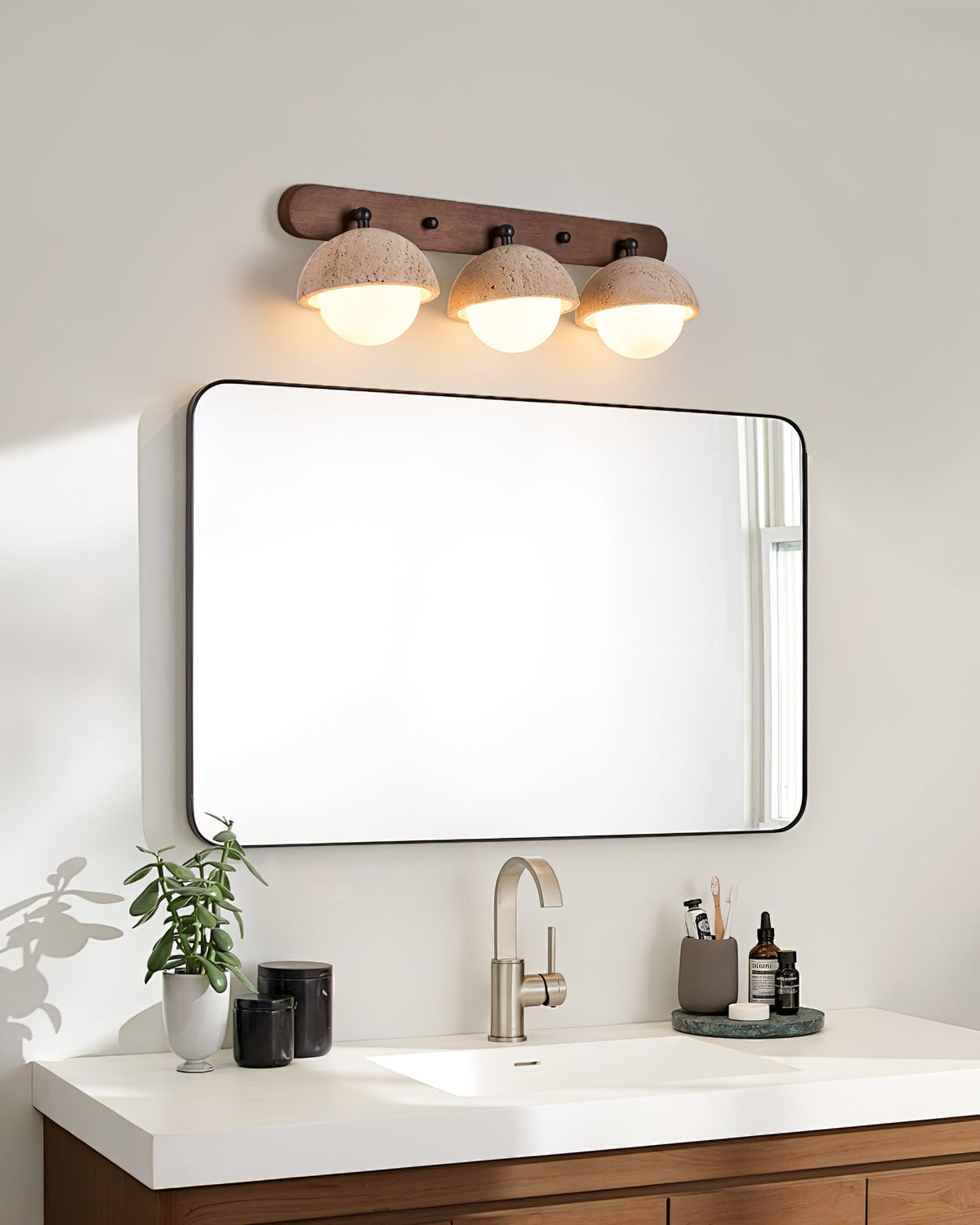 Three-dome Clérachic wall light above a rounded black-framed mirror, a white vanity top and a brushed-metal tap.