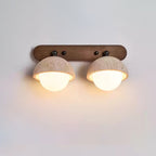 Close view of two lit travertine domes with frosted globes on a walnut backplate, a Clérachic wall light on a soft grey wall.