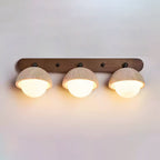 Three travertine domes with warm light glowing below each, on a long walnut bar; a Clérachic wall light on a pale wall.