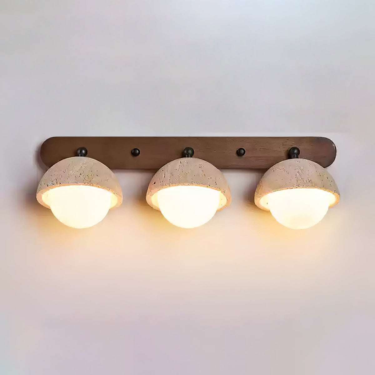 Three travertine domes with warm light glowing below each, on a long walnut bar; a Clérachic wall light on a pale wall.