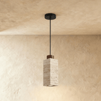 Clérachic's square travertine drum pendant hangs on a black cord, its wood cap sitting atop the veined stone column.