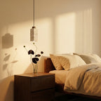 A round travertine drum pendant by Clérachic hangs close above a walnut nightstand with fresh-cut flowers.