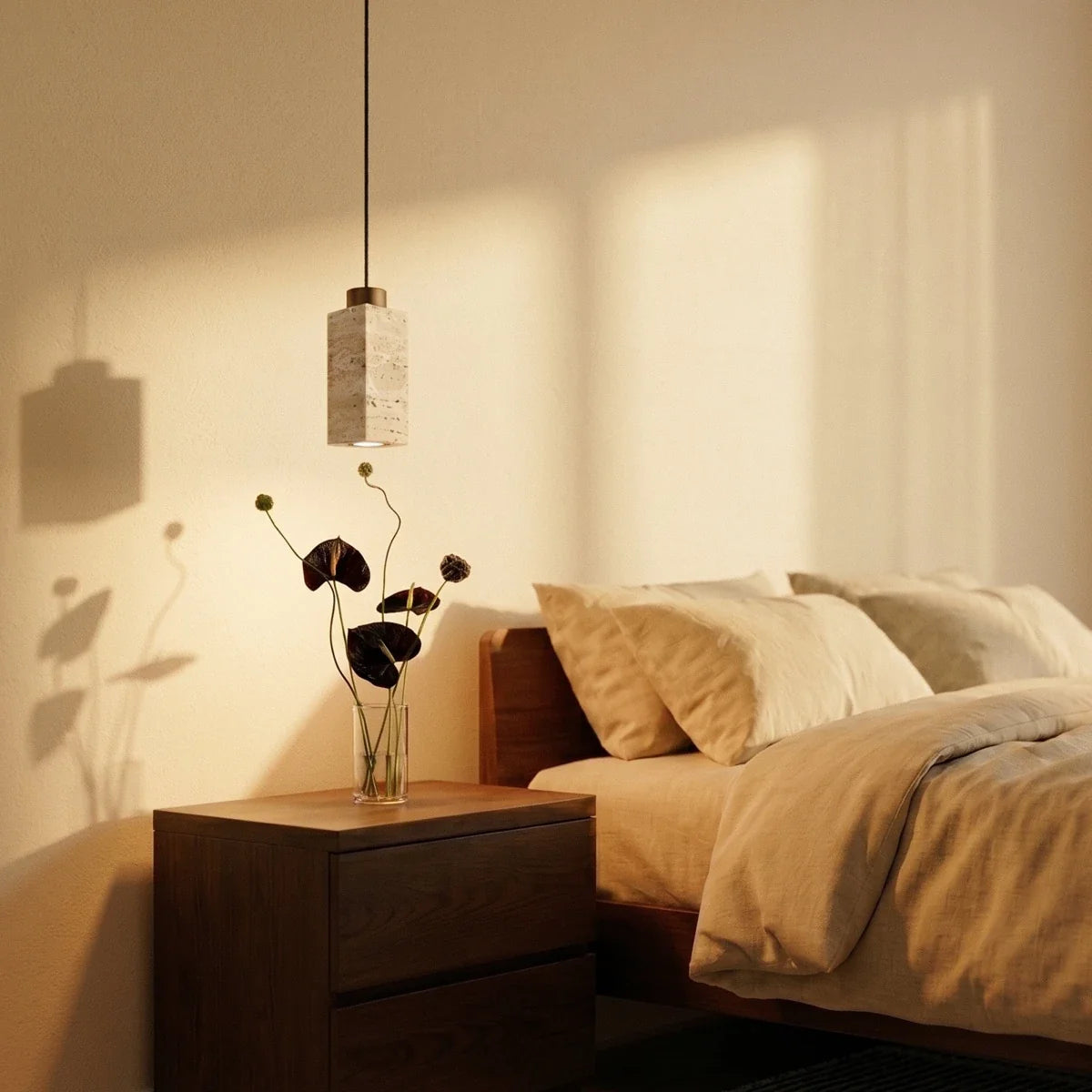 A round travertine drum pendant by Clérachic hangs close above a walnut nightstand with fresh-cut flowers.