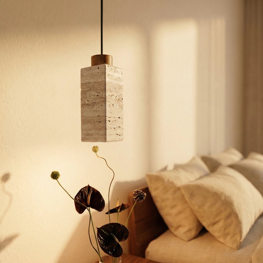 Clérachic's square travertine pendant hangs bedside, its stone cylinder glowing warm beside soft linen pillows.