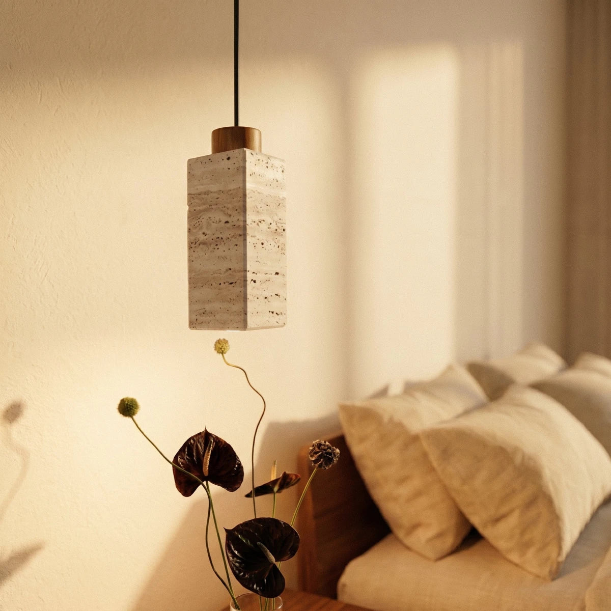 Clérachic's square travertine pendant hangs bedside, its stone cylinder glowing warm beside soft linen pillows.