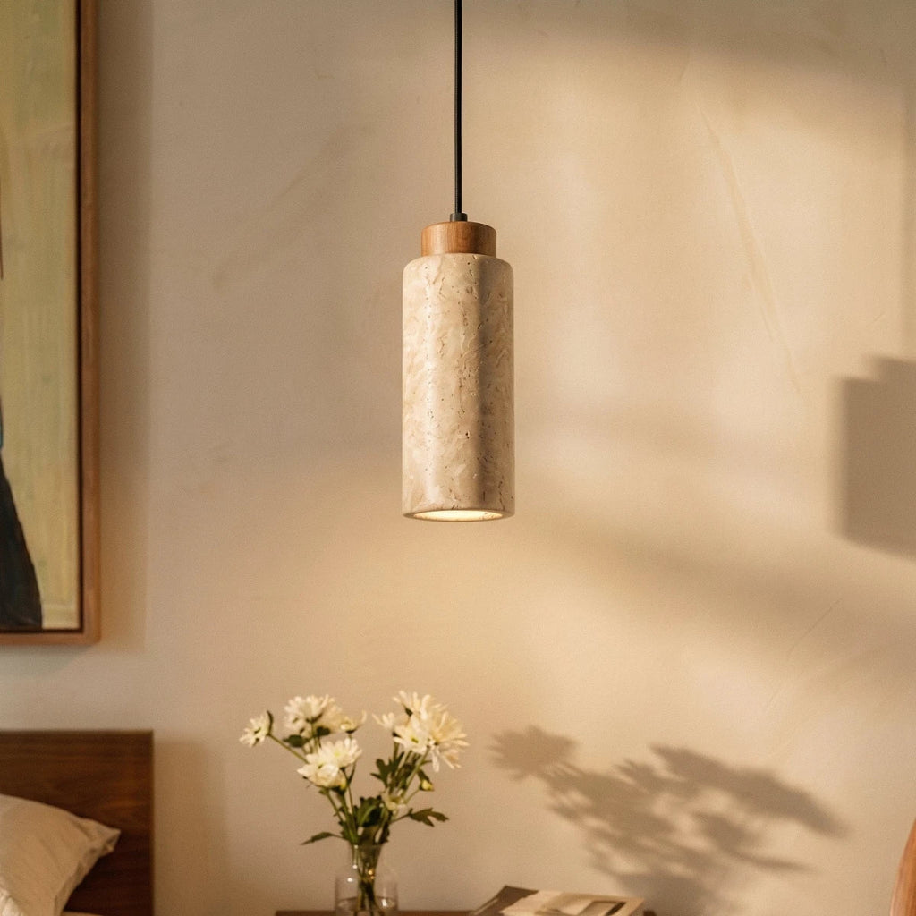A close-up of Clérachic's round travertine pendant shows its veined stone and wood cap beside bedside flowers.