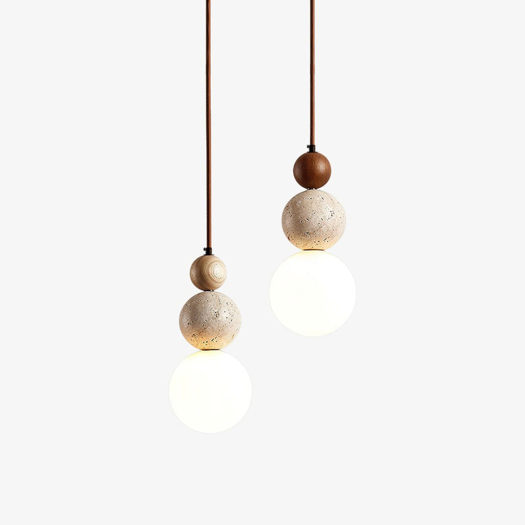 Two Clérachic pendant lights on a plain white backdrop, each a wood bead over a travertine ball and a white glass globe, one bead in dark walnut.