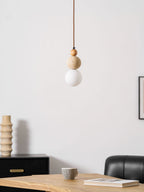 An unlit Clérachic pendant with a travertine ball and white globe, above a wooden table, with a ribbed vase and a black sideboard behind.