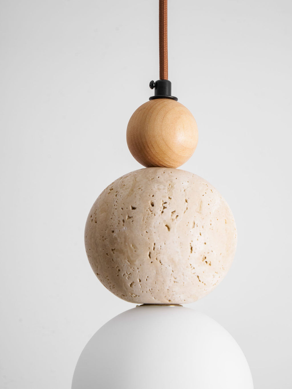 Close view of the wood bead, the pitted travertine ball and the white globe on this Clérachic pendant, with a black cord holder above.