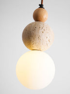 Close view of the lit white globe, the pitted travertine ball and the wood bead on this Clérachic pendant, on a grey backdrop.