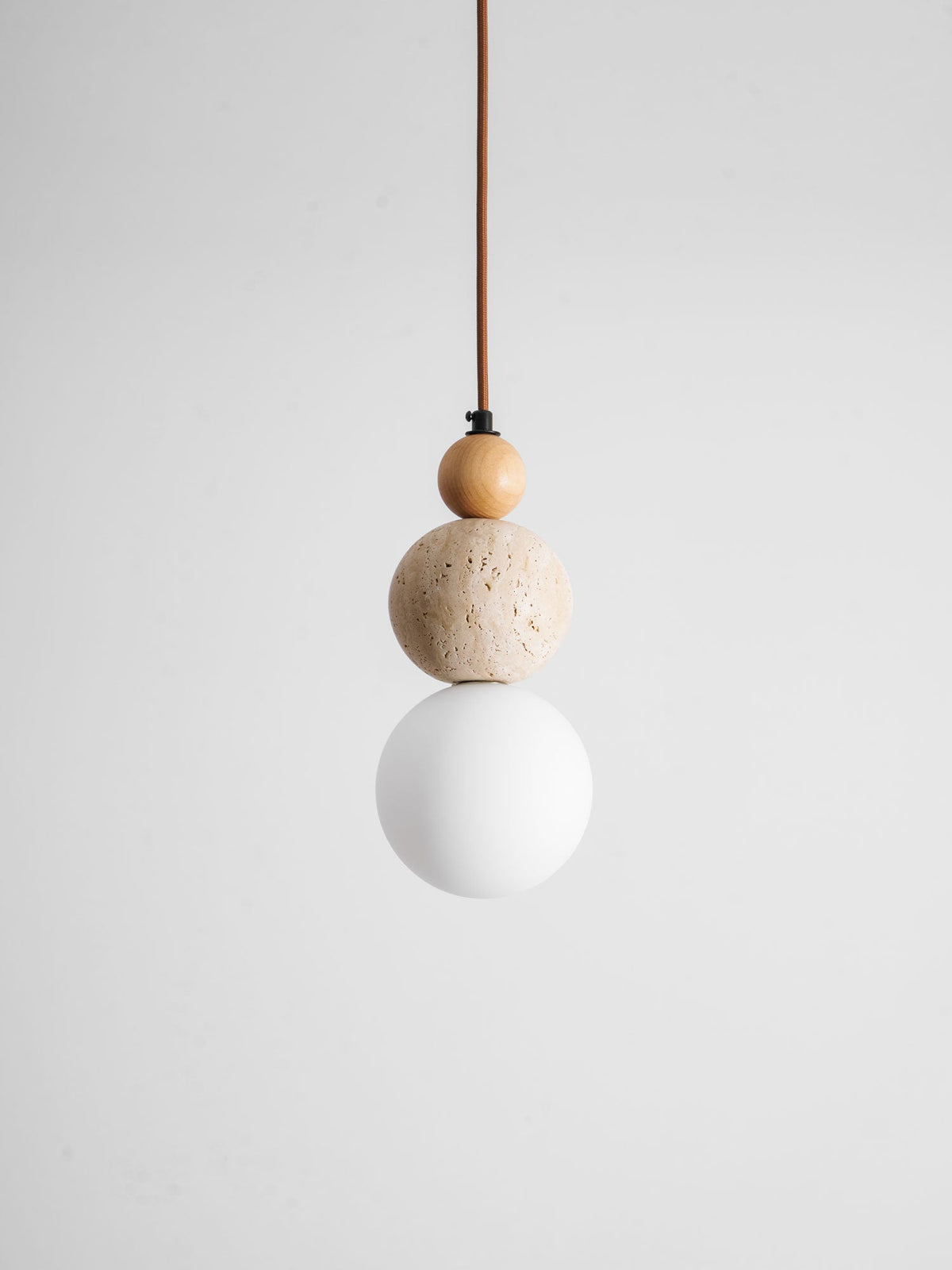 An unlit Clérachic pendant with a small wood bead, a travertine ball and a white globe hanging on a brown cord against grey.