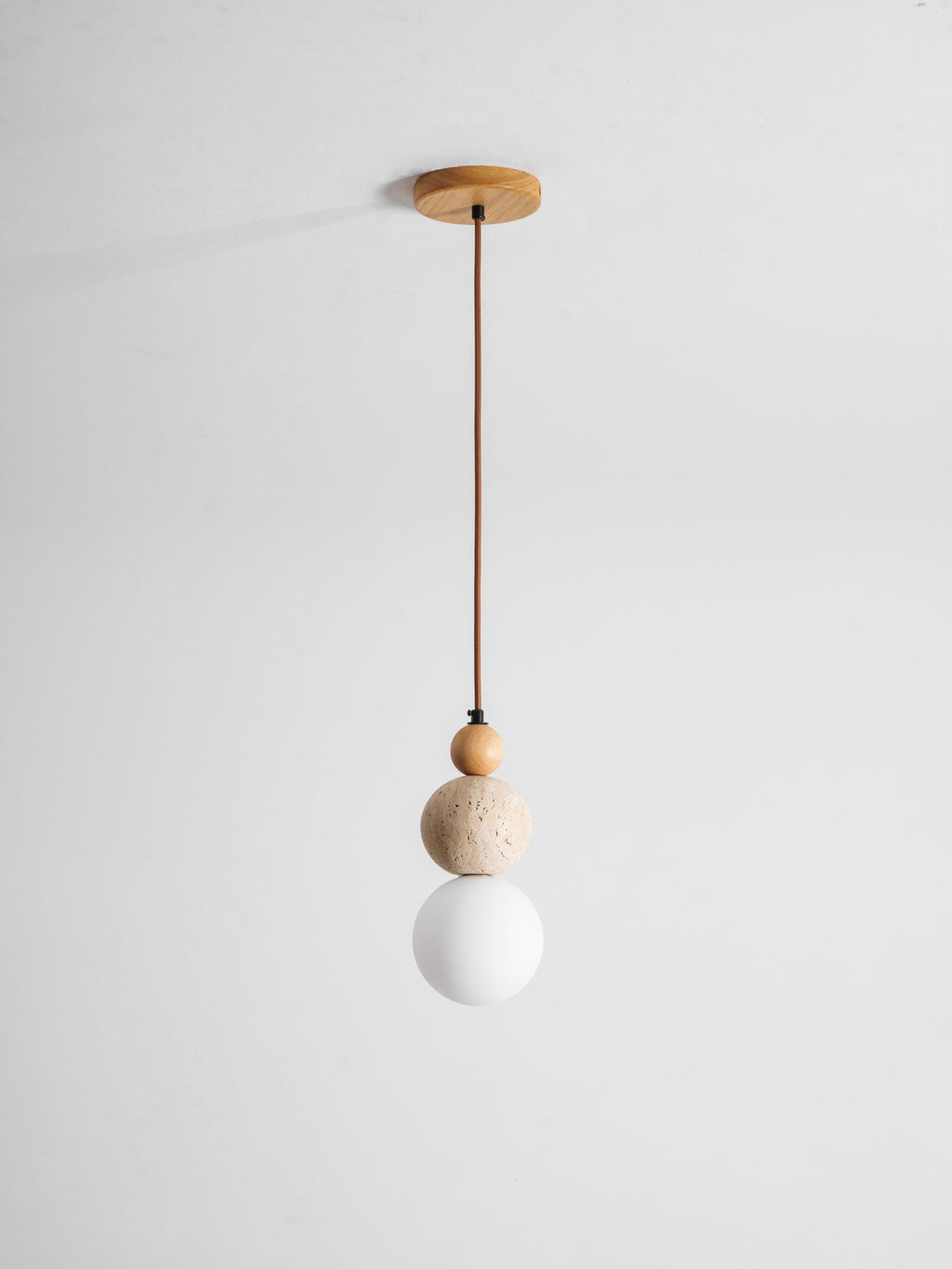 A Clérachic pendant on a brown cord from a round wood ceiling canopy, with a wood bead, travertine ball and unlit white globe.
