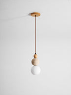 A Clérachic pendant on a brown cord from a round wood ceiling canopy, with a wood bead, travertine ball and unlit white globe.