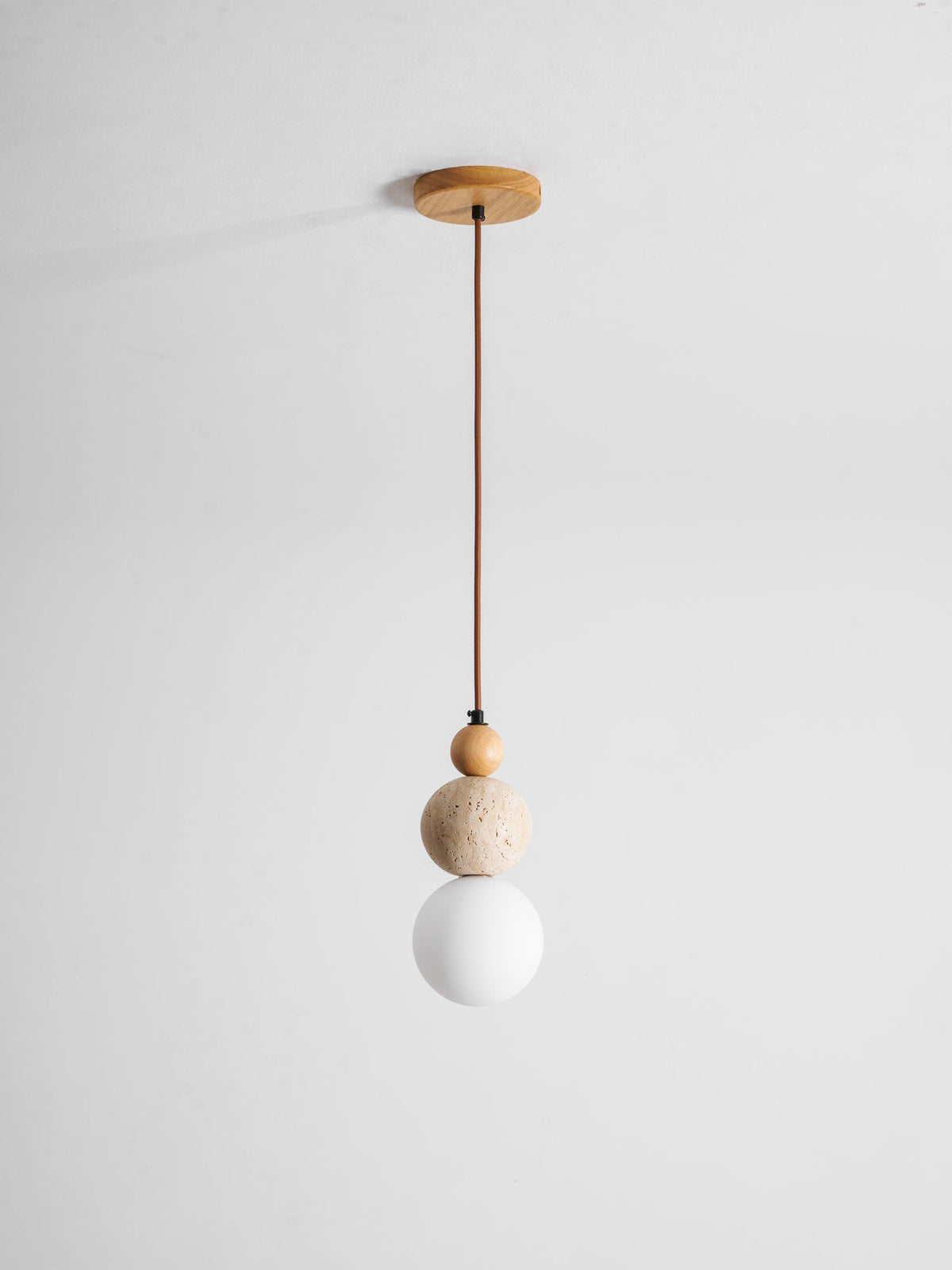 A Clérachic pendant on a brown cord from a round wood ceiling canopy, with a wood bead, travertine ball and unlit white globe.