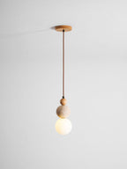 A Clérachic pendant on a brown cord from a round wood canopy, with its white globe glowing warm under the travertine ball.