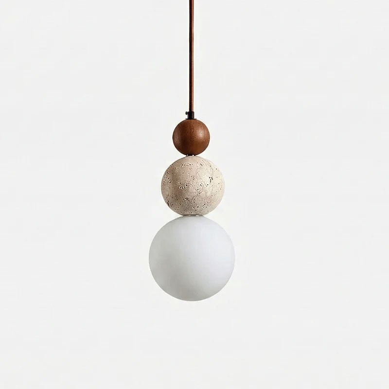 A Clérachic pendant on a plain light backdrop, with a dark walnut bead above a pitted travertine ball and a matt white globe.