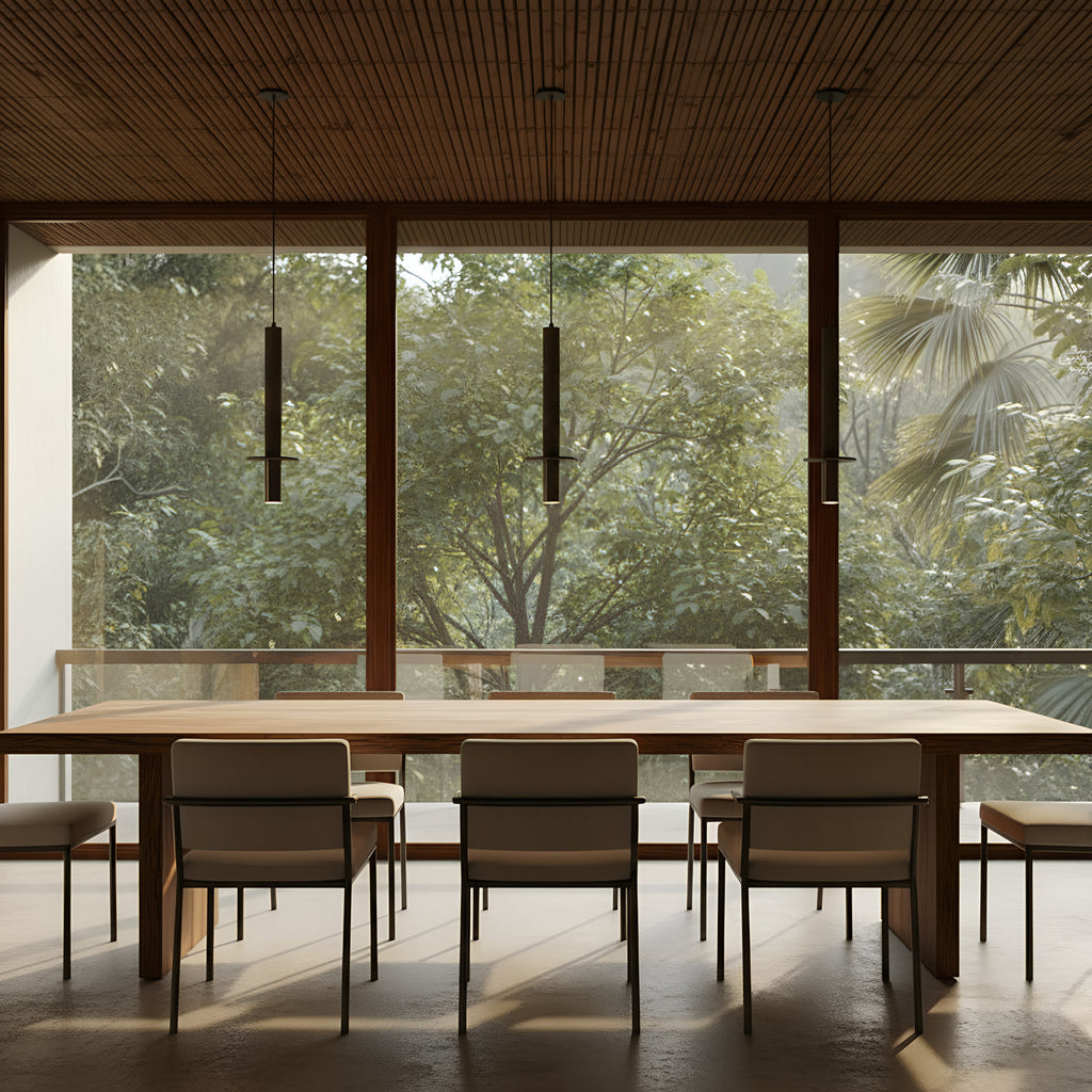 Three Clérachic travertine pendants in a row above a single long timber dining table, a glazed wall onto greenery behind