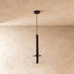A Clérachic pendant light's ribbed dark cylinder hangs above a small steel disc and downlight, cord bare.