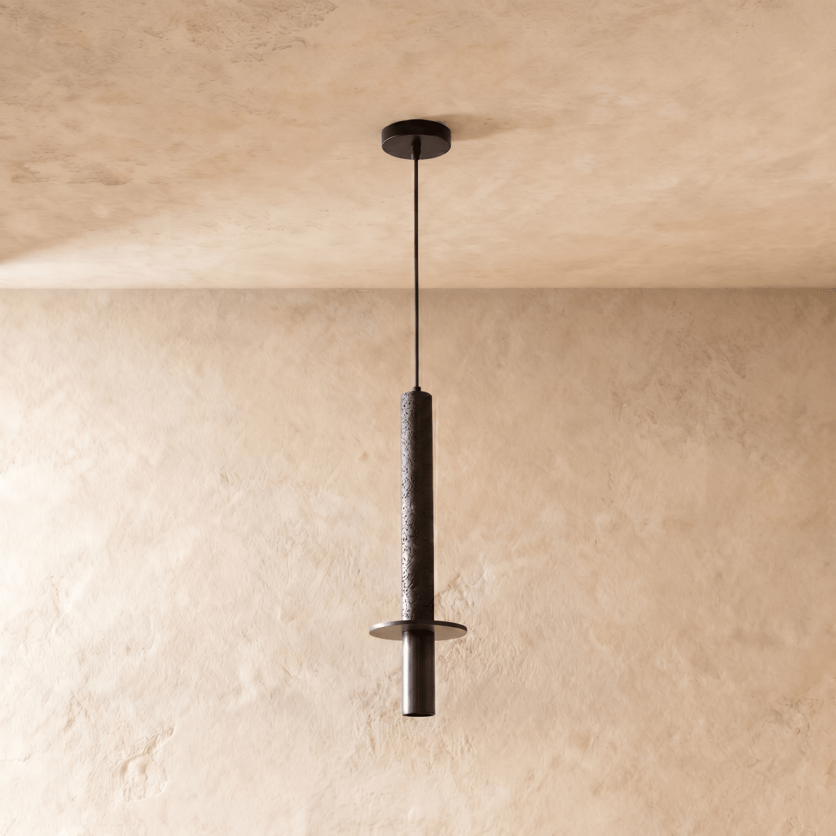 A Clérachic pendant light's ribbed dark cylinder hangs above a small steel disc and downlight, cord bare.