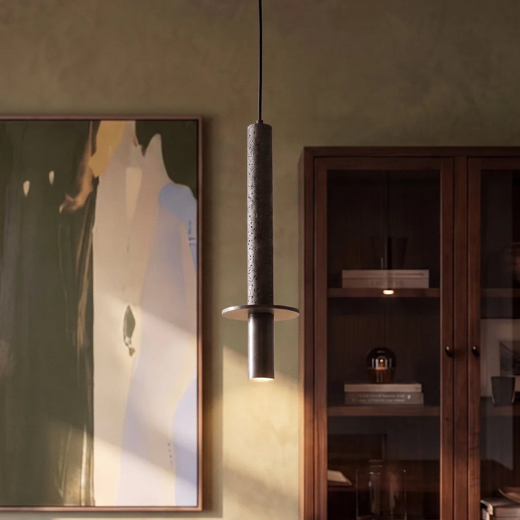 A Clérachic pendant light's textured cylinder glows beside an abstract painting and a walnut display cabinet.