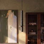 A Clérachic pendant light's textured cylinder glows beside an abstract painting and a walnut display cabinet.