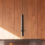 A Clérachic pendant light's stone-textured cylinder glows softly against a warm wood-paneled wall.