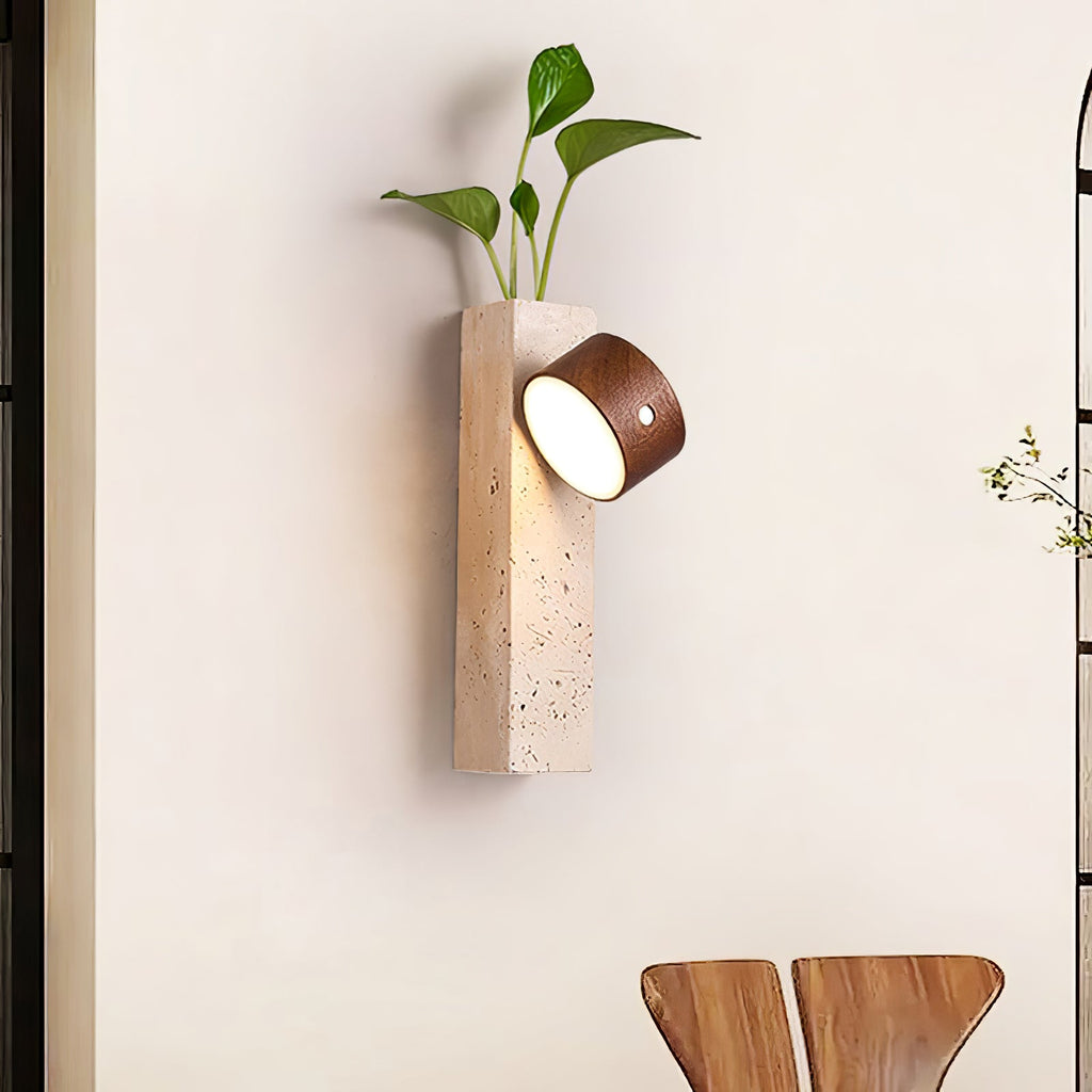 A Clérachic dark walnut wall light on a Yellow Travertine block with a green plant growing from the top, beside an arched window.