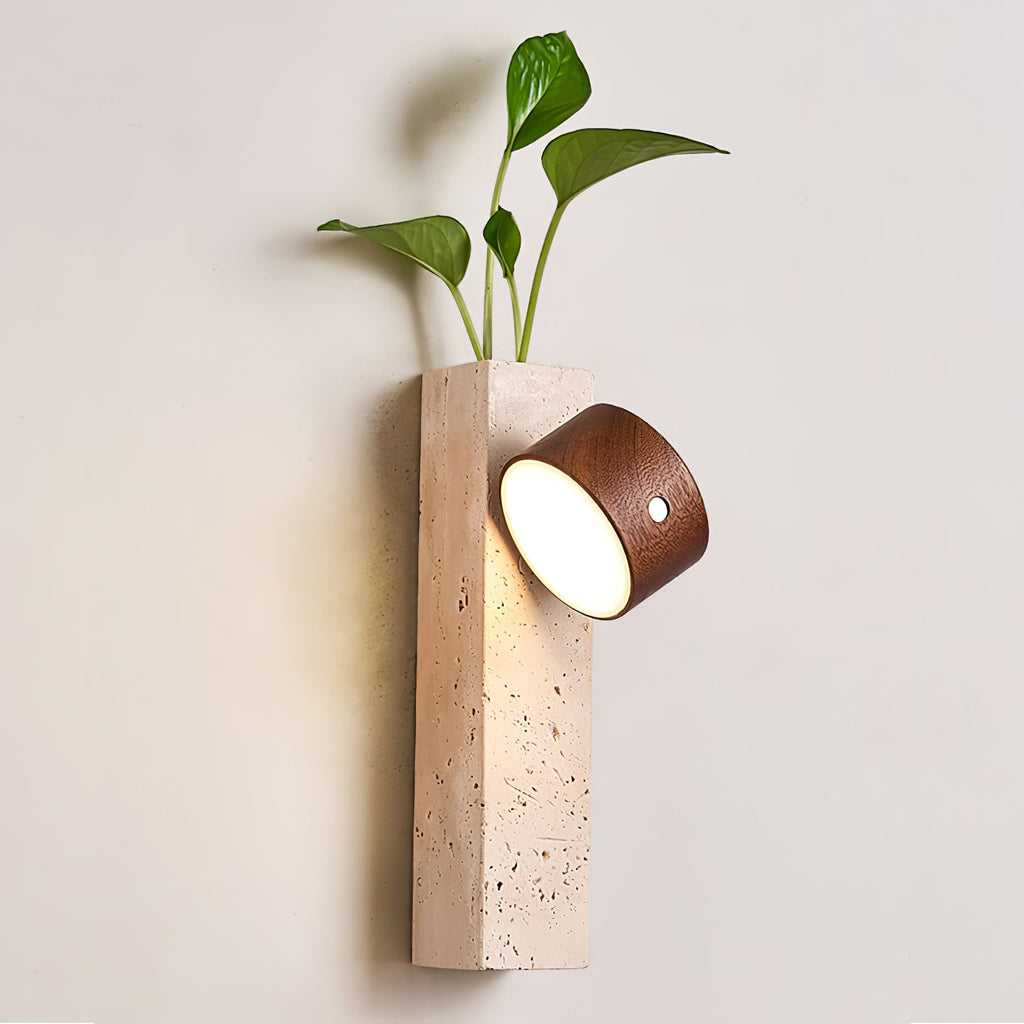 Nearer view of a Clérachic Dark Walnut & Yellow Travertine wall light, its tilted lit head glowing beside a leafy plant.