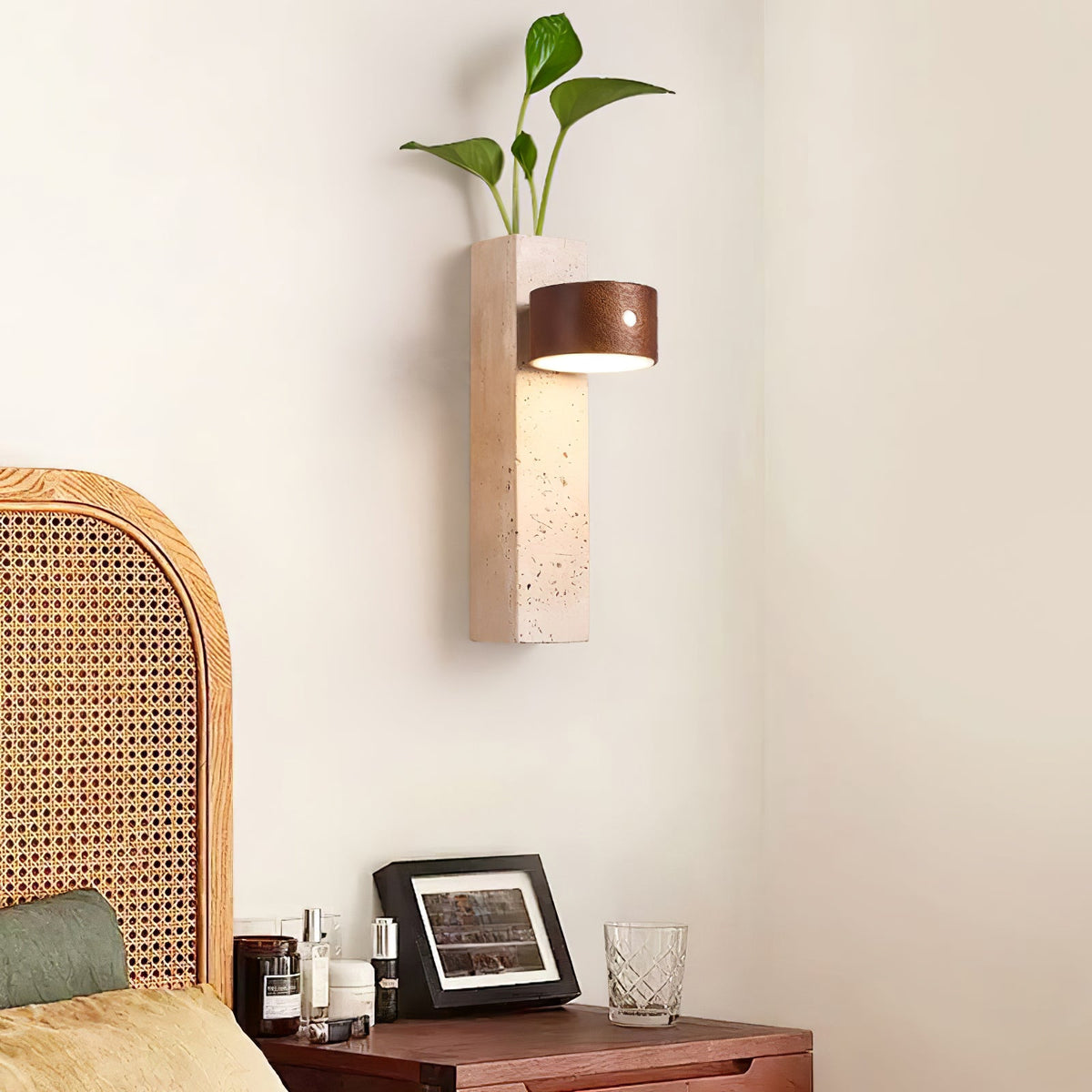 A Clérachic wall light with its walnut head turned sideways, hung on a cream wall above a rattan-headed bed and a bedside table.