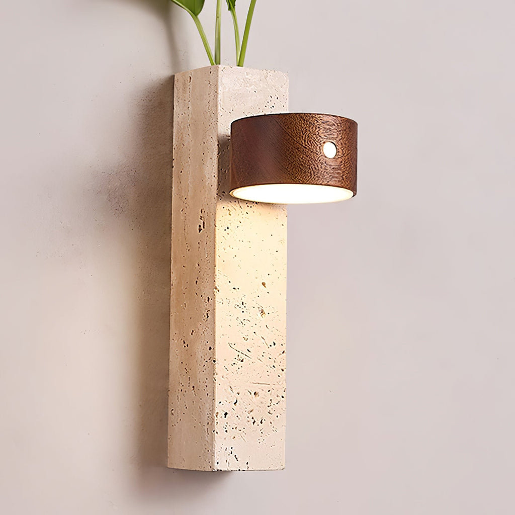 Close view of a Clérachic wall light with its dark walnut head lit downward, showing the pitted travertine block below.