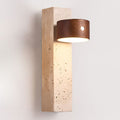 Close view of the travertine block, with its natural pits and holes, under the lit walnut head of this Clérachic wall light.