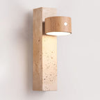 A Clérachic wall light in Wood & Yellow Travertine, with a pale wood round head lit downward over the pitted stone block.