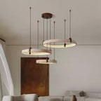 Seen from below, three lit travertine rings from Clérachic hang over a cream sofa, beside a rust-coloured canvas on a pale wall.
