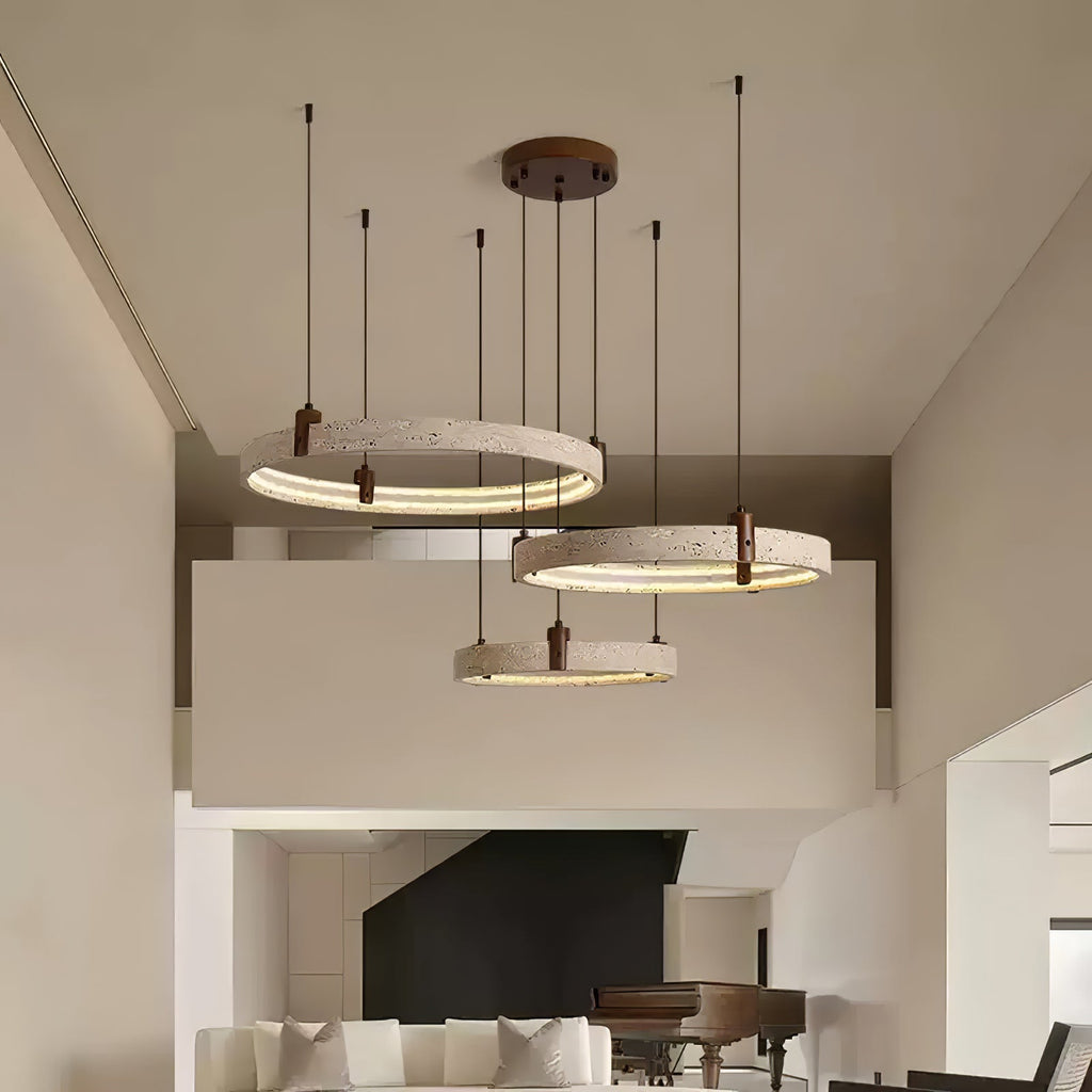 Three travertine rings from Clérachic hang at staggered heights in a double-height room, with a balcony and a black fireplace behind.