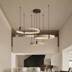 Three travertine rings from Clérachic hang at staggered heights in a double-height room, with a balcony and a black fireplace behind.