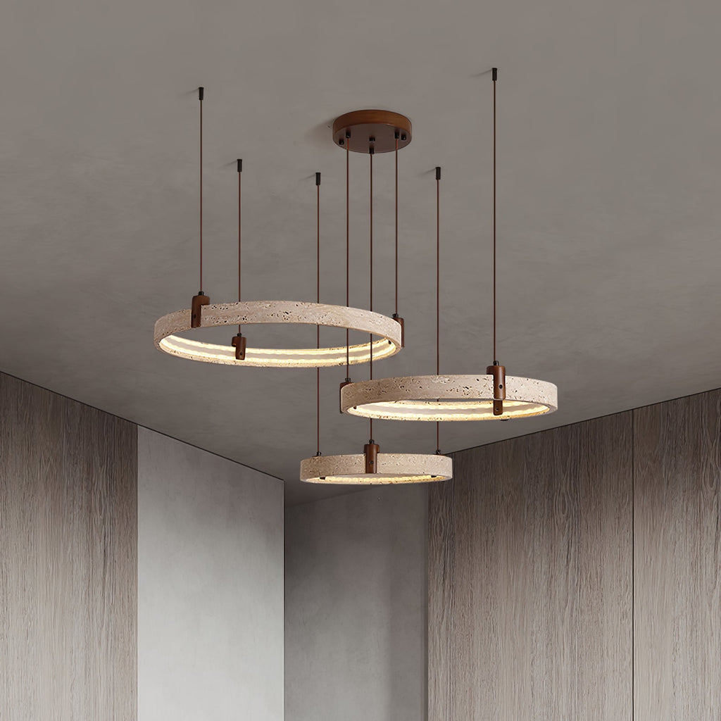 Looking up at a Clérachic pendant of three travertine rings, the canopy and cords reach a plain ceiling above wood-panelled walls.
