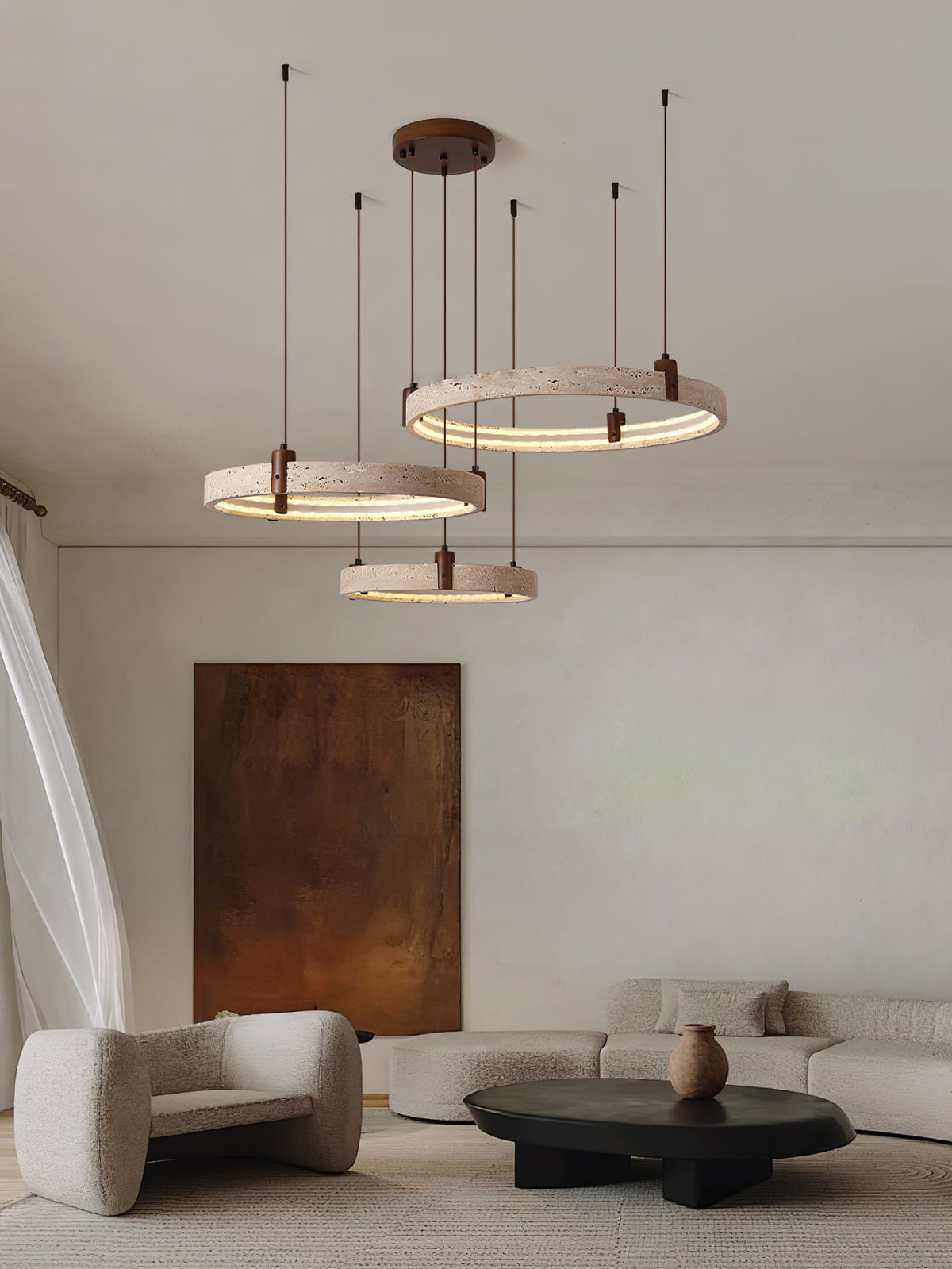 A Clérachic pendant of three travertine rings floats above a black coffee table and a boucle armchair, with a rust canvas behind.
