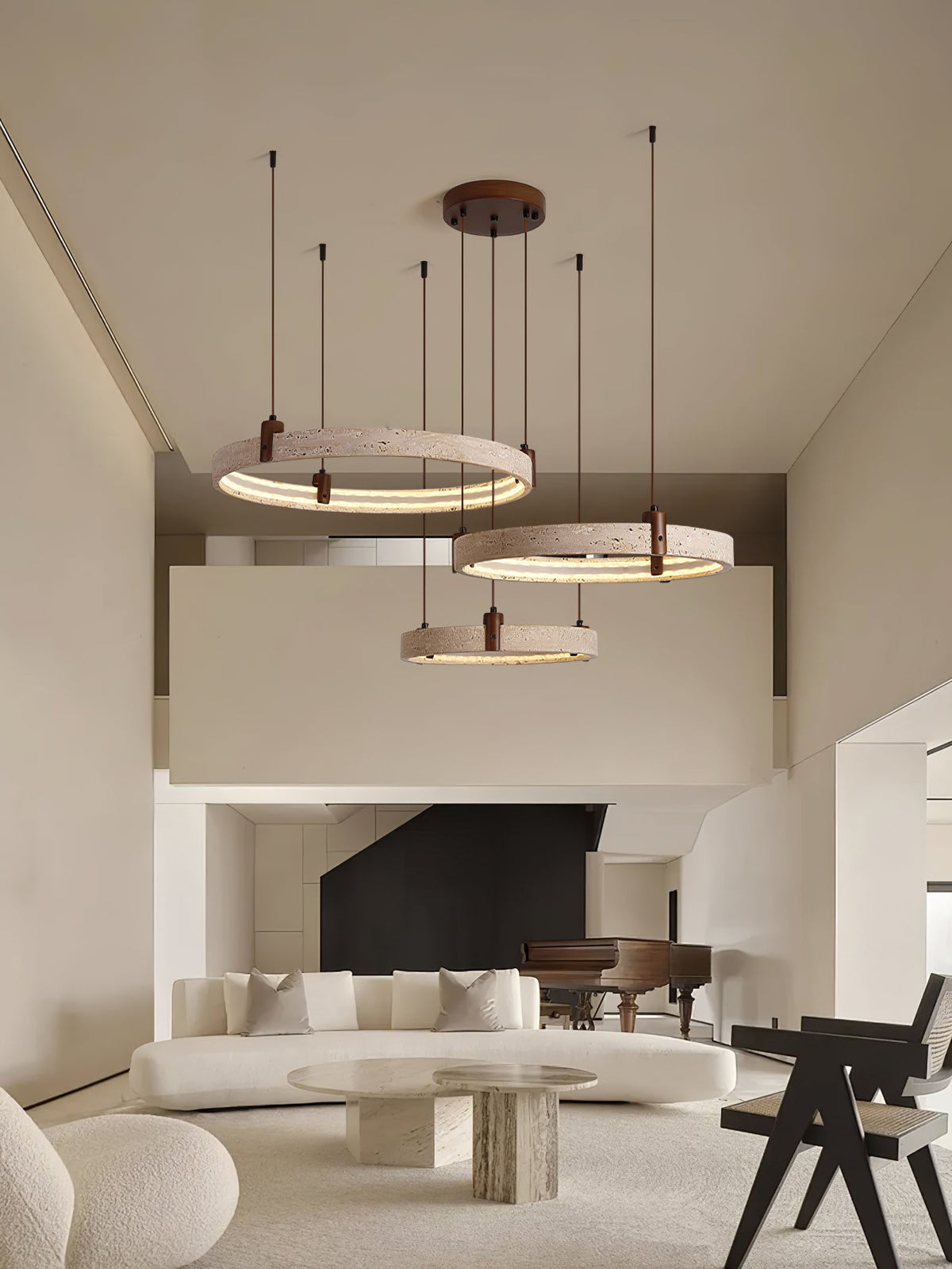 Three glowing travertine rings from Clérachic hang in front of a mezzanine, over a curved sofa and a stone coffee table.